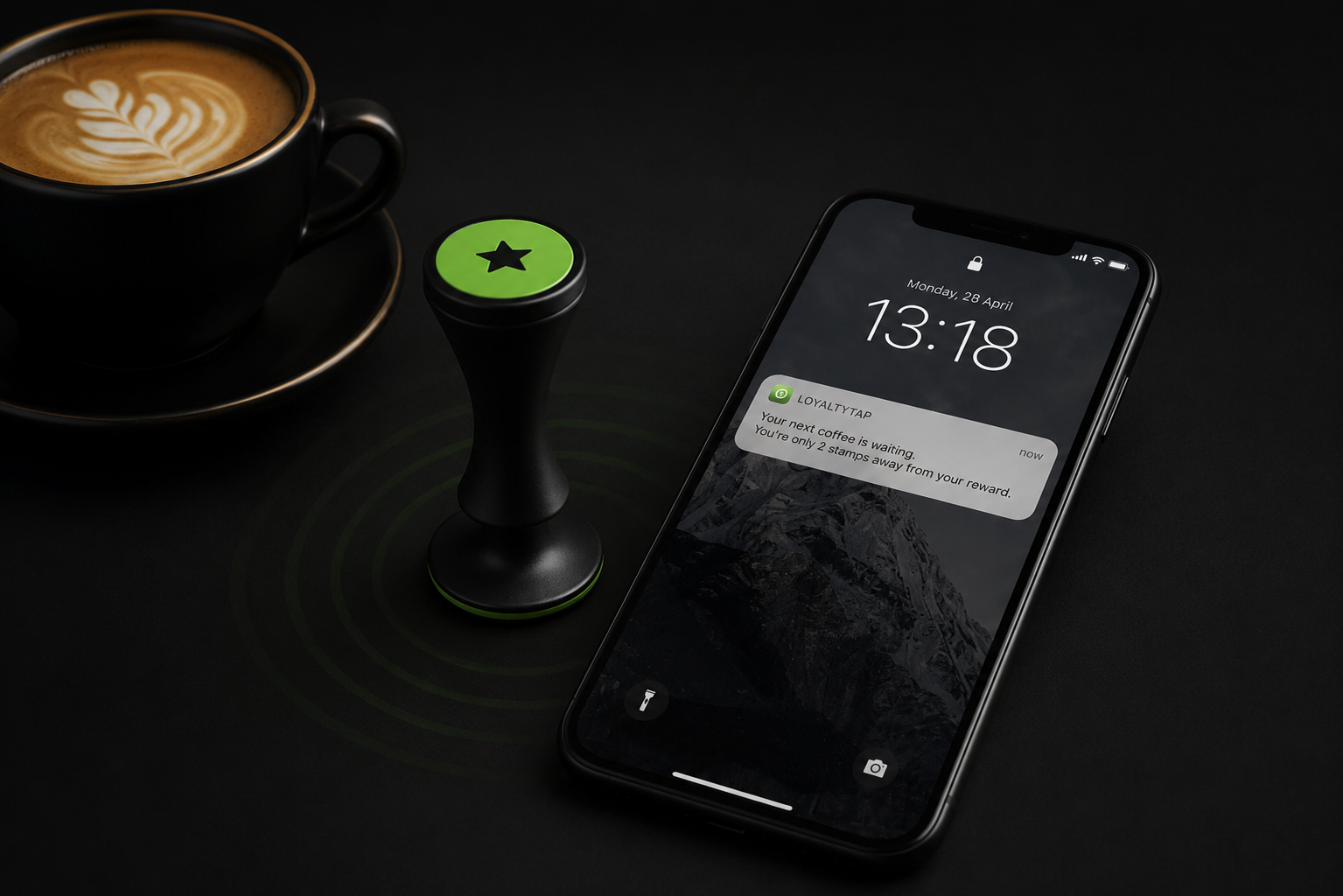 A black LoyaltyTap NFC stamp with a glowing green ring on a dark café counter next to a coffee cup, with a smartphone showing a lock-screen loyalty notification